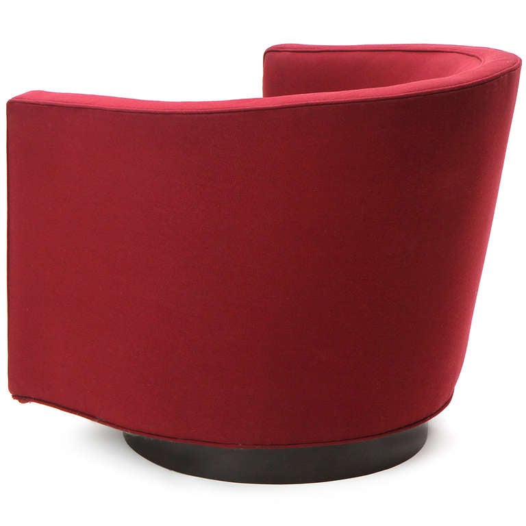 A swiveling upholstered barrel-back lounge chair that retains its original crimson fabric, having an encircling form rising from a circular disc base.
