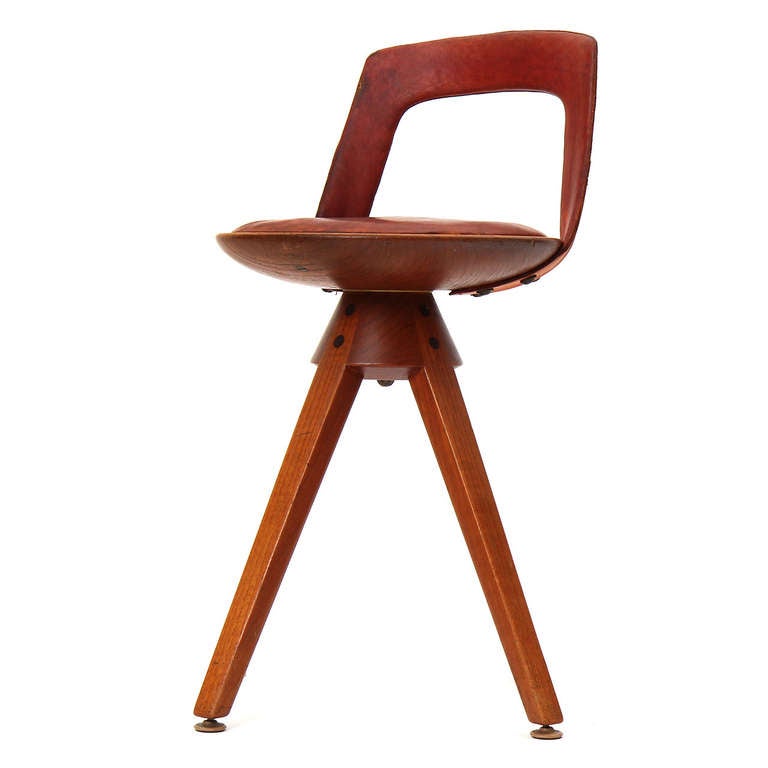A rare swivel seat stool with a low leather backrest and seat cushion, on splayed teak tapered legs.