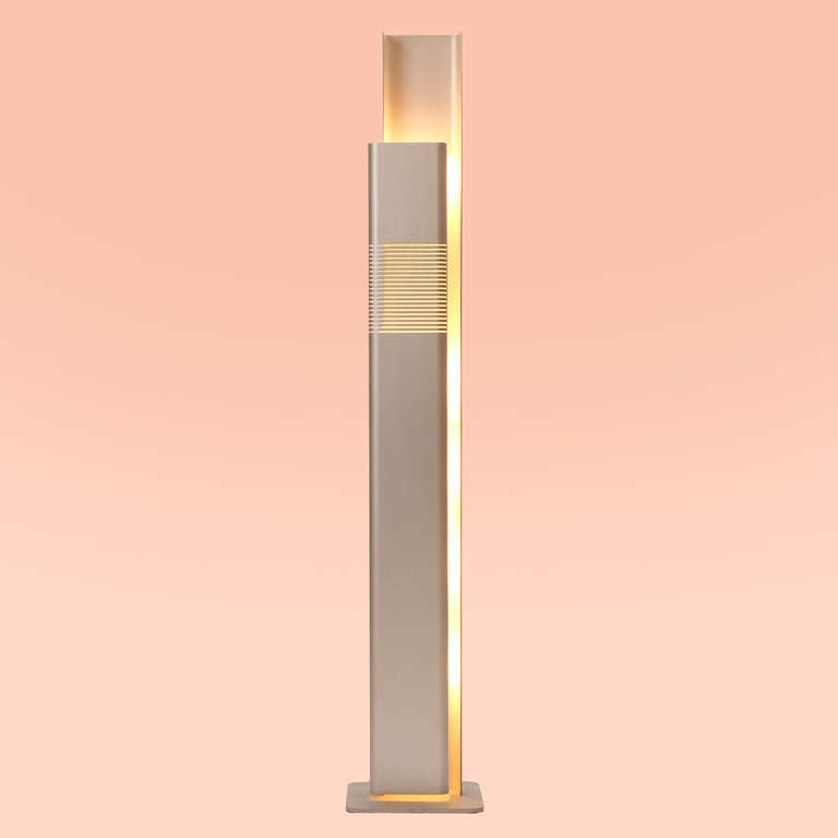 A floor lamp comprised of two facing channeled aluminum elements. The front ribbed panel swivels to allow access to bulbs. Base measures 12