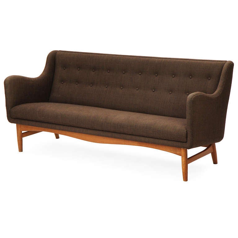 A sculptural sofa having an exposed teak frame and dowel turned legs, with a tightly upholstered seat and a button tufted back in the original woven brown wool.