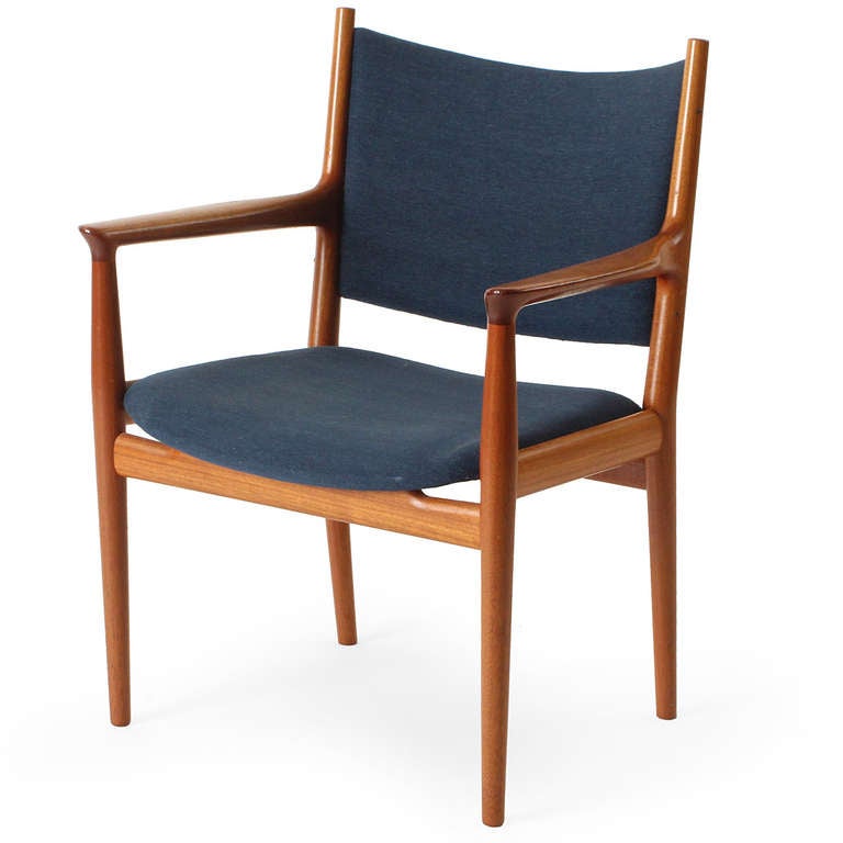 An arm chair devoid with an exposed teak frame and a gently curved seat and back retaining original upholstery.