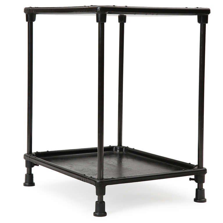 A well-crafted two-tiered industrial table rendered in  patinated steel and iron, with each shelf having raised and rolled edges, and legs that rise from generous bell-shaped feet.