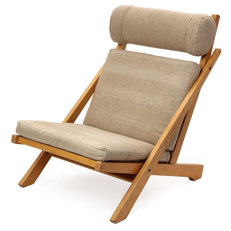 An architectural low lounge chair having an exposed beech slat-backed frame with flag halyard weaving and soft, light grey linen upholstery; the headrest is adjustable.