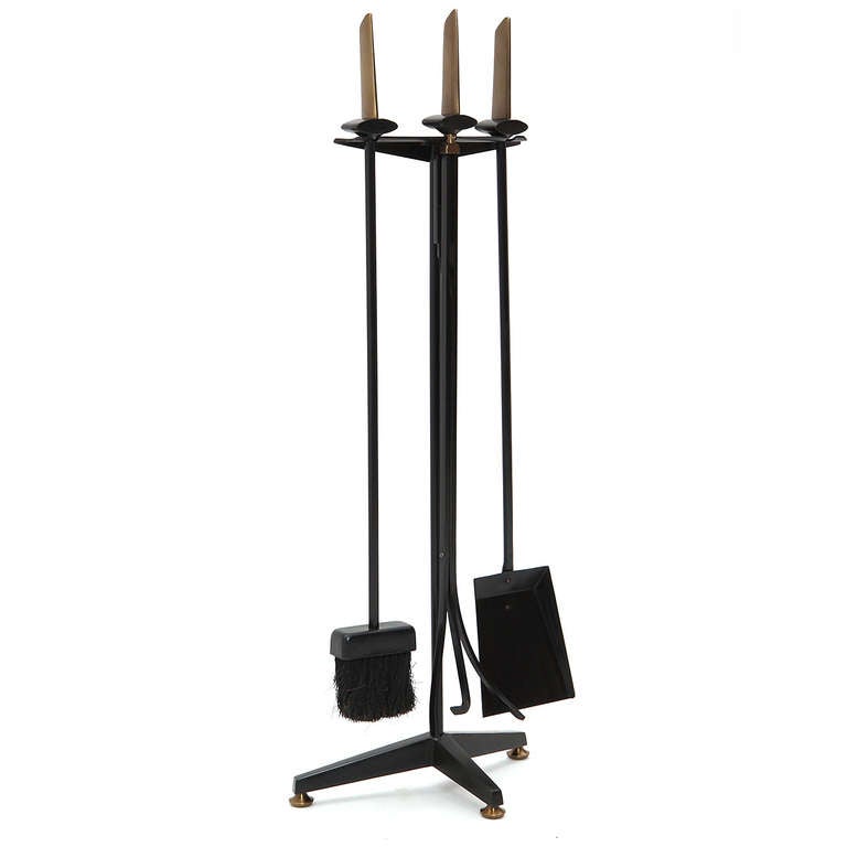 An elegant and sculptural set of fire tools in iron and brass that hang from an architectural tri-footed stand.