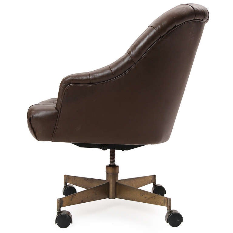 A comfortable and elegant adjustable swiveling executive armchair, the seat having tufted upholstery and floating on a cruciform brass-toned steel base with casters.