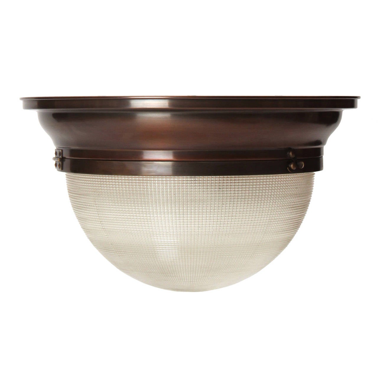 An elegant and finely manufactured flush-mount industrial light fixture that can function as a wall sconce or ceiling light, having a stepped patinated brass body and a domed prismatic glass shade.