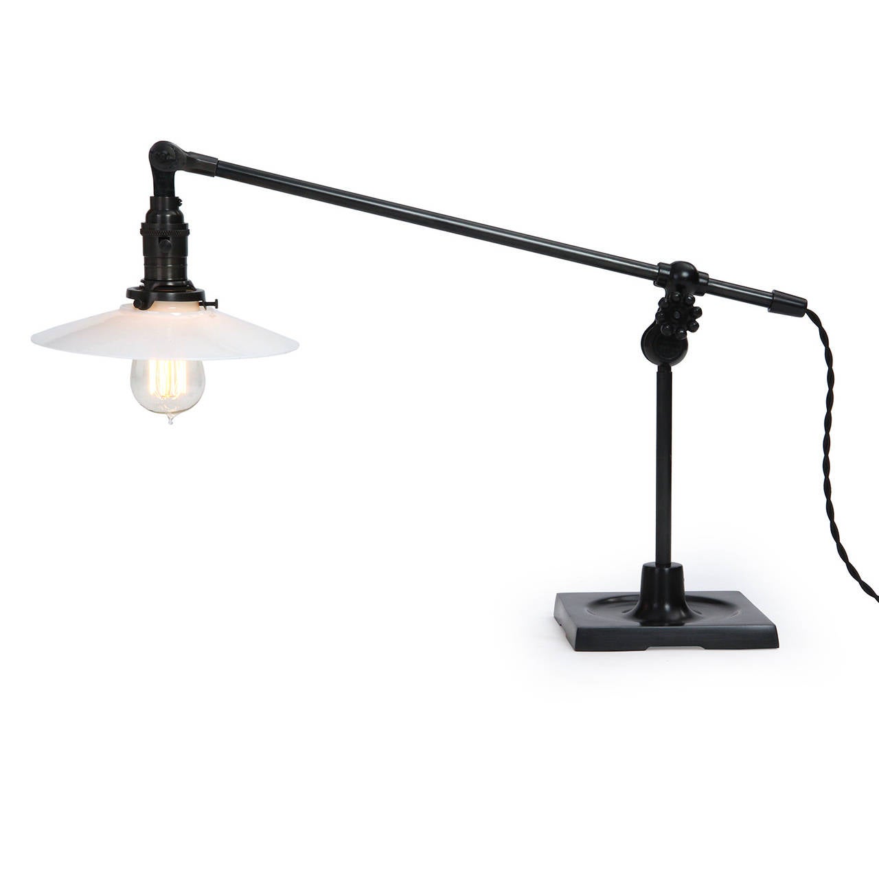 A spare, superb and impeccably detailed articulating desk lamp in patinated bronze having a sculptural square bronze base and a thin hemispheric milk glass shade.