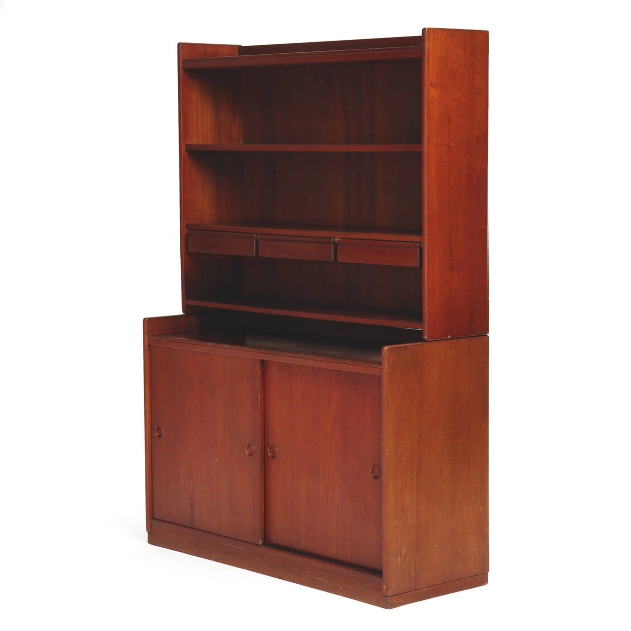 An elegant, finely crafted and spare modular floor cabinet in solid rich teak having an upper section with adjustable open shelves and three floating drawers perched on a base with two sliding doors accessed by recessed finger pulls.
