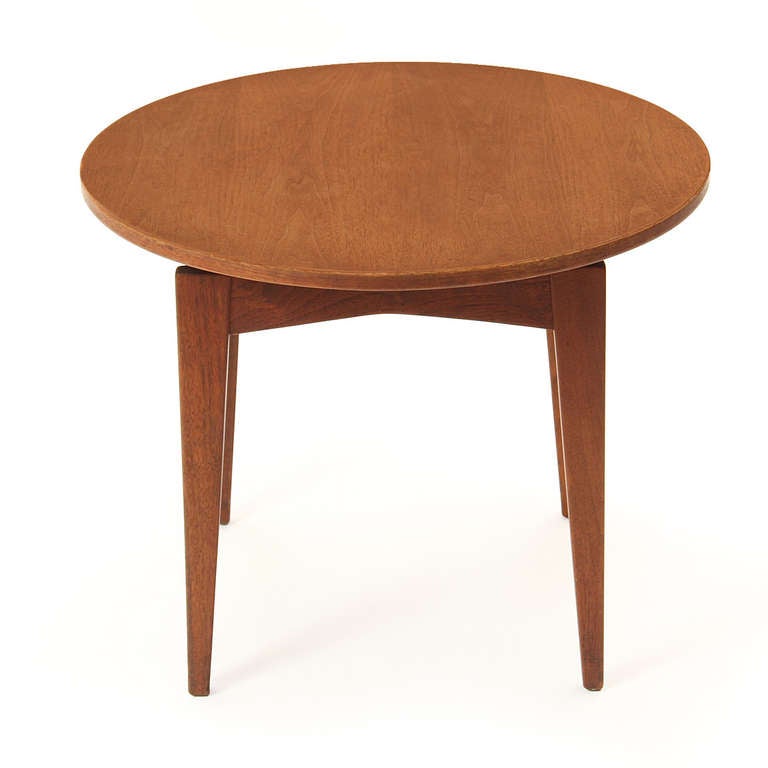 An end table in solid walnut featuring four tapered legs supporting a floating round top.