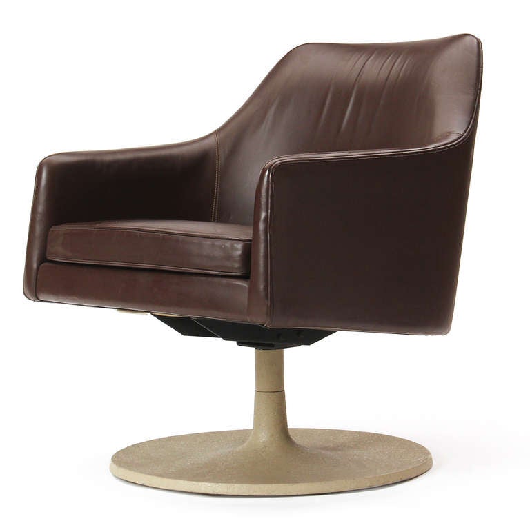 An upholstered swiveling lounge chair in leather with a tilt mechanism on a metal disc base. 
  