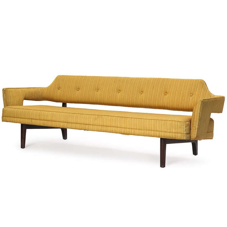 A dramatic and sculptural sofa having a one piece body upholstered in golden silk with a striking elevated floating back and exposed architectural base.