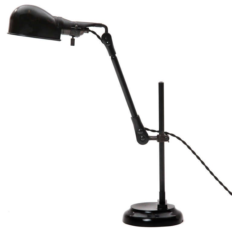 An adjustable desk lamp in polished patinated steel having a pivoting shade attached to an articulating arm that rises from a slender stem anchored by a weighted base.