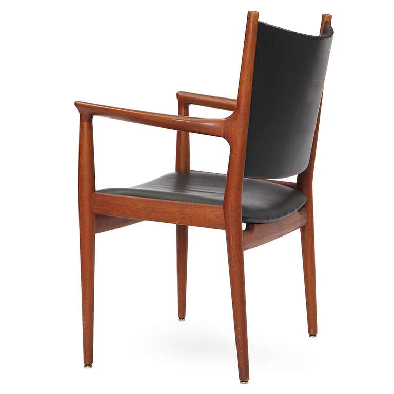 A handcrafted and elegant armchair devoid of extraneous detailing, having an exposed solid teak frame and a gently curved seat and back in leather upholstery.
      