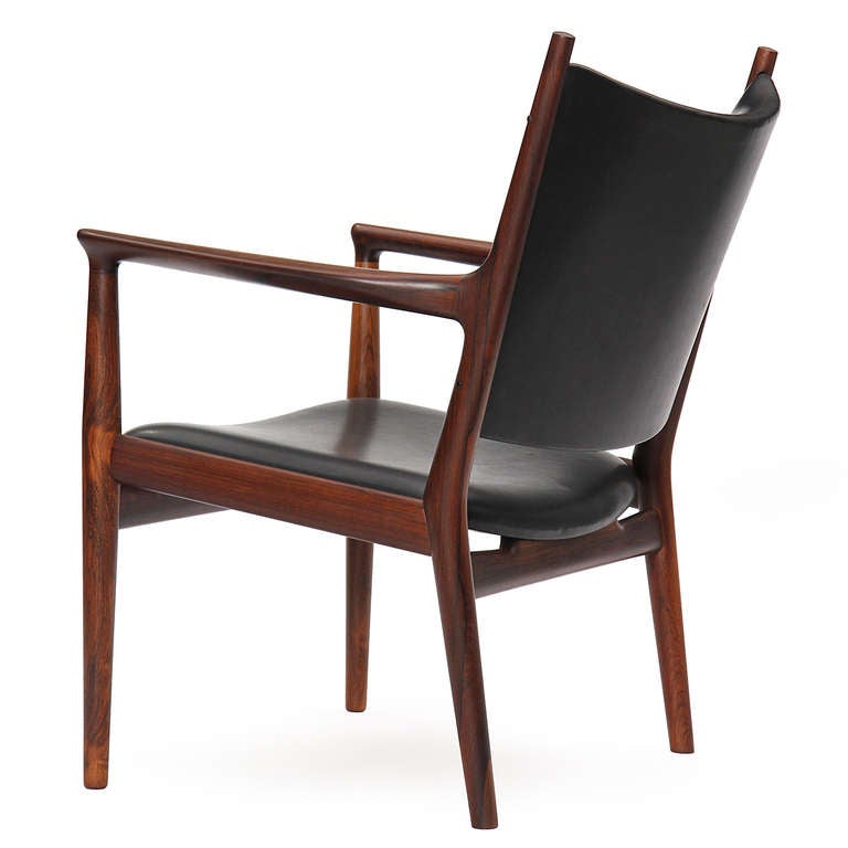 A pair of impeccably crafted rare armchair devoid of extraneous detailing, having an exposed solid rosewood frame and a gently curved seat and back in black leather. 
Designed by Hans Wegner and made by Johannes Hansen cabinetmaker.