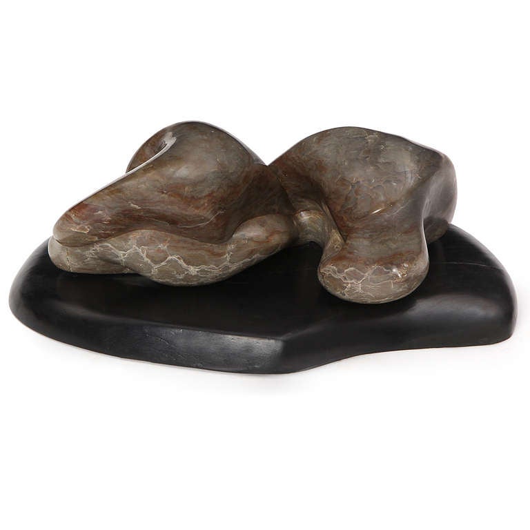 An abstract sculpture carved of richly figured marble and mounted on an organically shaped lacquered wooden base.