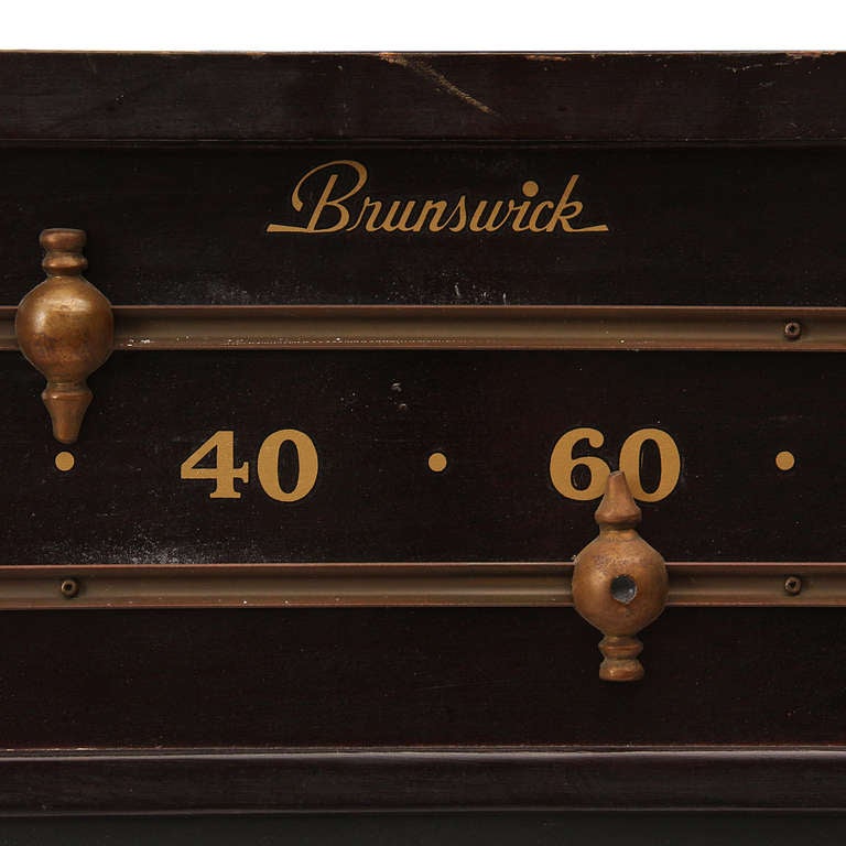 A vintage billiards scoreboard by Brunswick in lacquered wood and slate with gold lettering and brass slides.