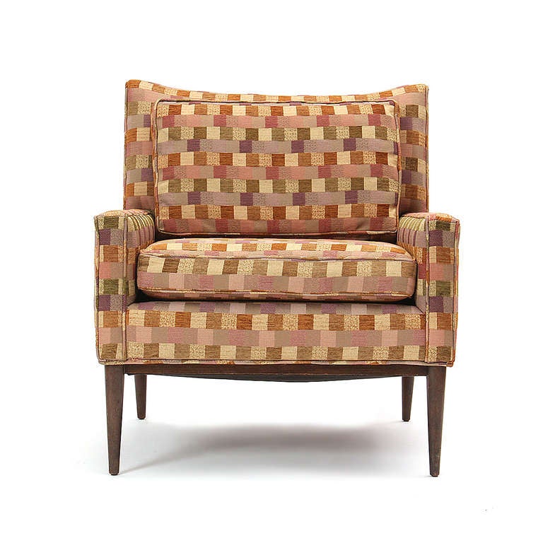 An upholstered and tailored club chair on walnut legs that retains its original multicolored check-patterned fabric.