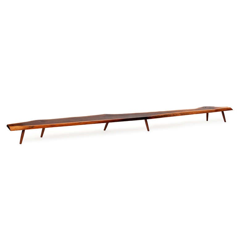 A magnificent studio-made low table or bench crafted from a single dramatic twelve-foot long slab of beautifully figured and toned live-edge walnut which floats on six staggered dowel-form legs.