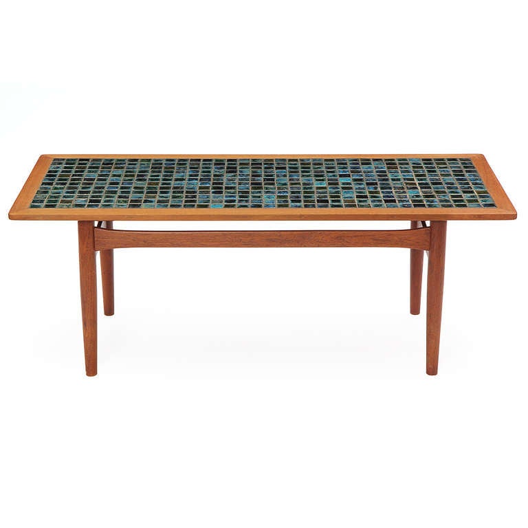 A well-crafted coffee or low table in teak having an architectural structure supporting a rectangular top inlaid with rich and expressive hand-made iridescent ceramic tile.
