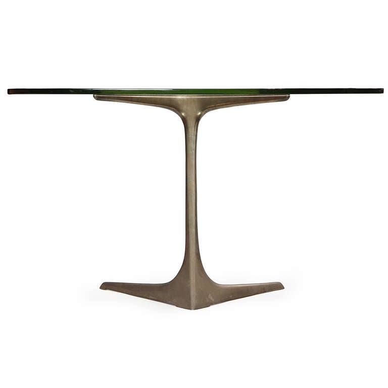 A dramatic, rare and sculptural table having a cantilevered solid bronze-nickel base supporting a triangular-shaped thick glass top.