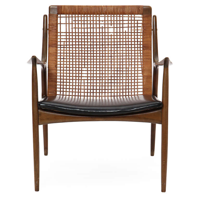 An elegant and expressive pair of armchairs having an open sculptural frame, leather-wrapped seat and a caned back.