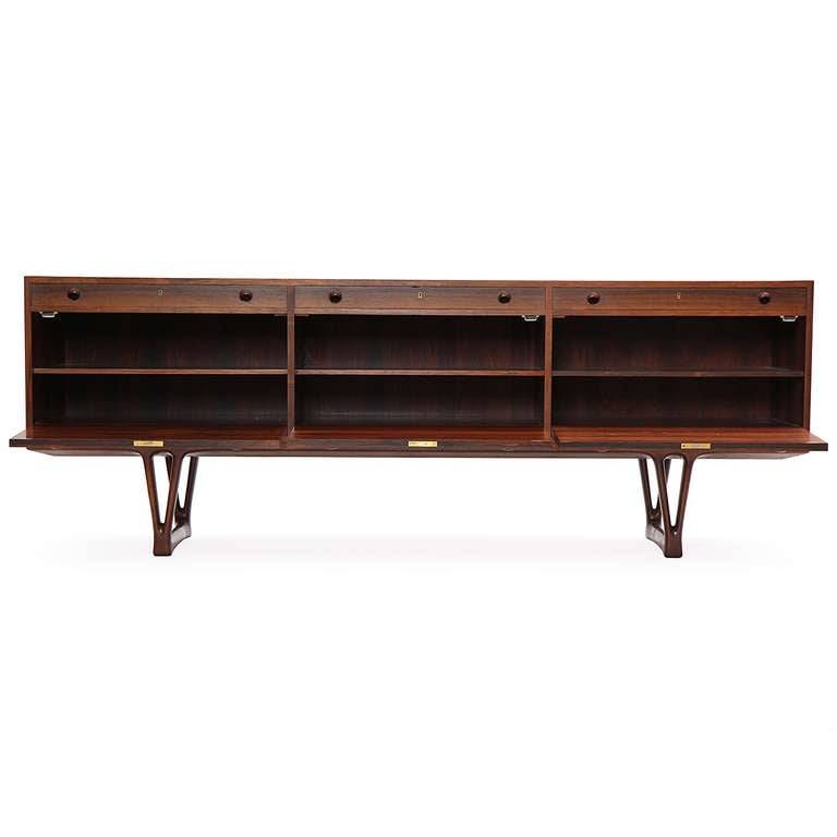 An elegant and expressive fully finished credenza in vividly grained rosewood having three drawers and three drop front doors concealing shelving; case atop sculptural Y-form sled legs.