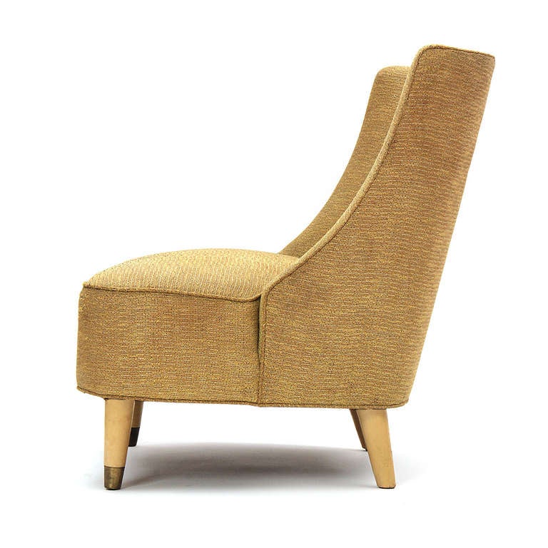 An expressive and highly comfortable slipper chair featuring pale, brass-tipped dowel legs and fine, button-tufted upholstery.