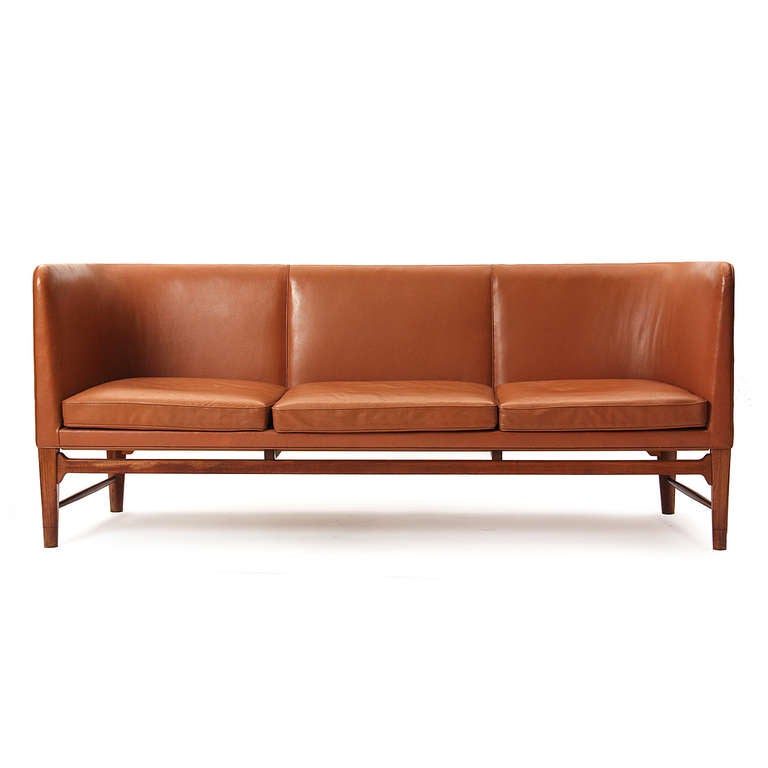 A unique sofa with an even-arm, U-shaped backrest and leather upholstery, on Cuban mahogany, square-to-round, tapered legs. One of two made for the Town Hall of Sollerod, Denmark.