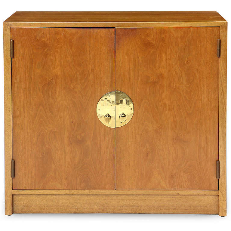 An rectilinear light walnut two-door cabinet having Chinese-influenced hardware and open and adjustable shelves, the form sitting on a plinth base.