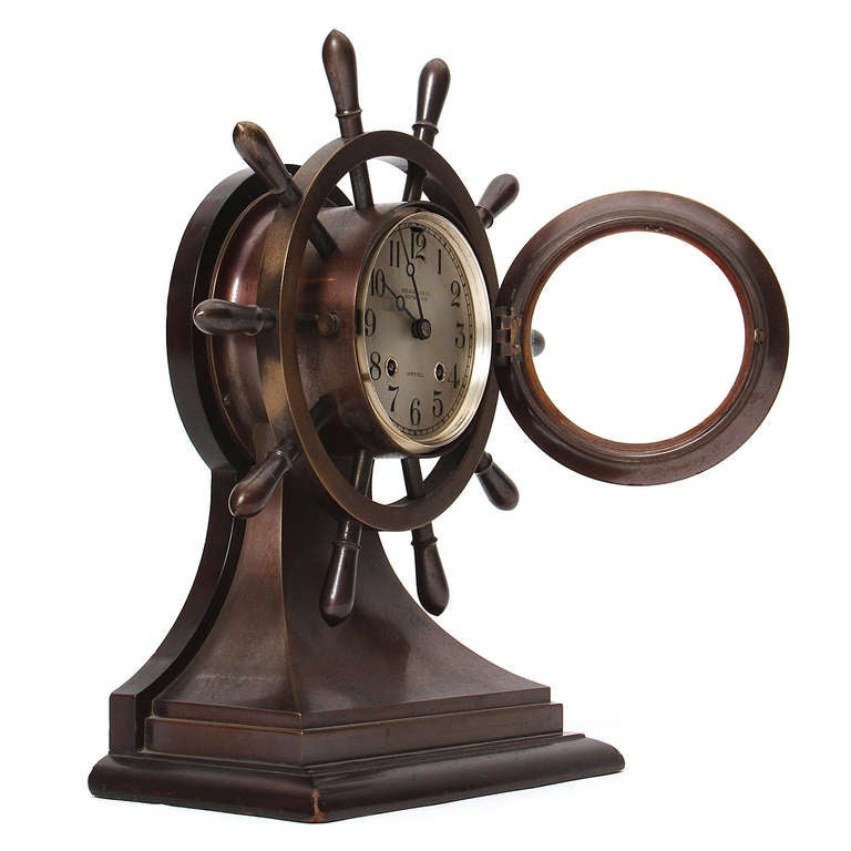 A finely crafted bronze clock in the form of yacht steering wheel made by Chelsea Clock Company, Boston, Massachusetts, having a hinged bezel, silvered dial with Arabic numerals, eight-day time and ship's bell striking lever escapement movement.