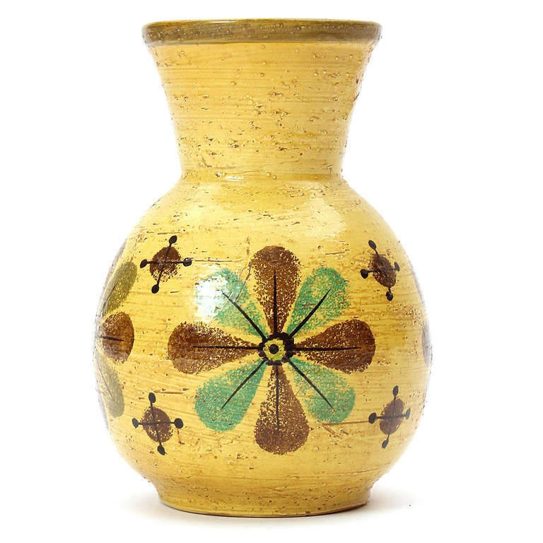 A hand-thrown ceramic vessel with a rustic mustard glaze and painted floral decoration.