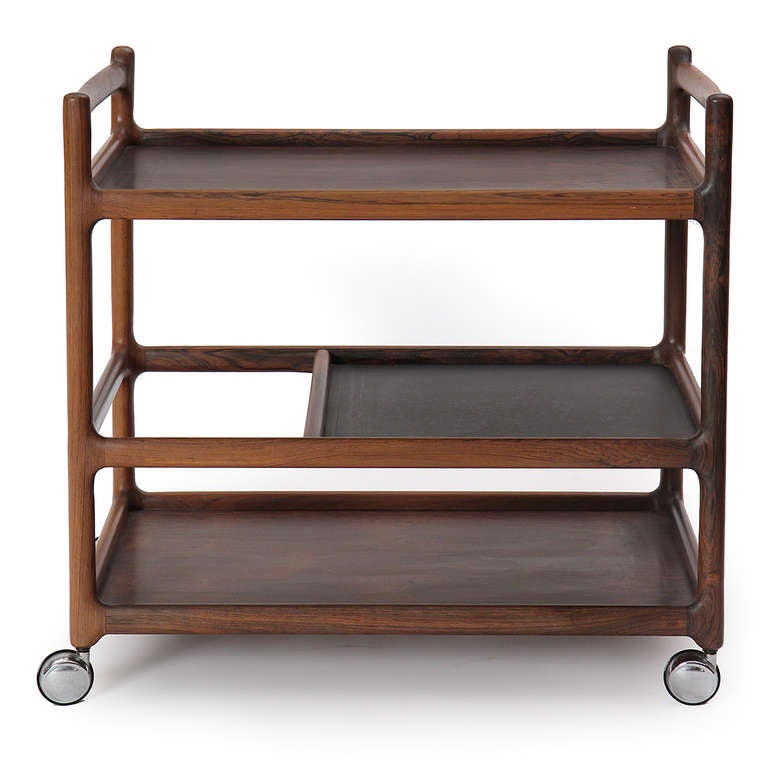 A sculptural rolling cart in solid rosewood on chromed casters having three shelves, the middle shelf partially cut back to accommodate standing bottles.