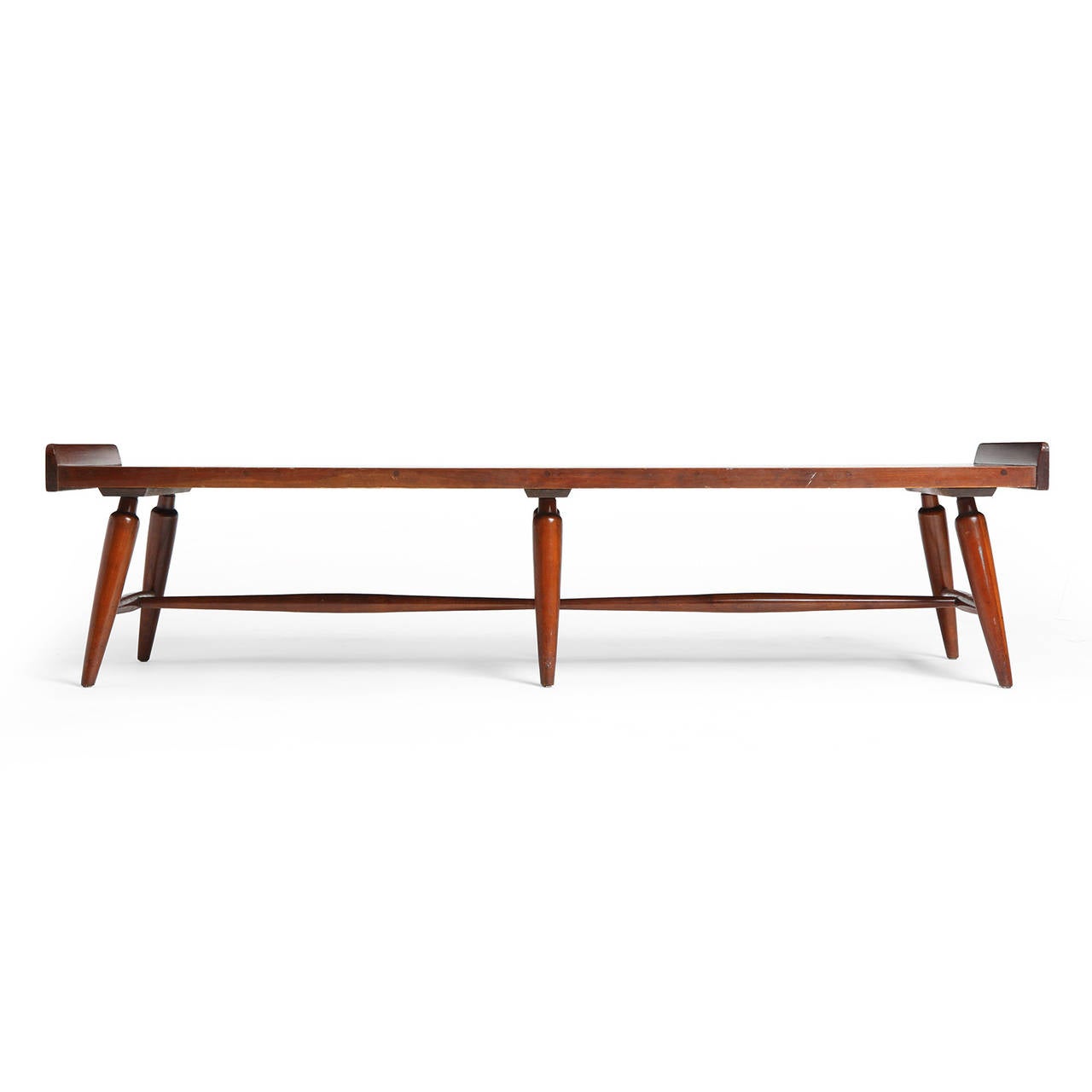 A walnut low table having a long rectangular top with raised end rails resting on a six-legged base with turned legs  and stretchers. The legs attach to the top with a through tenon detail.