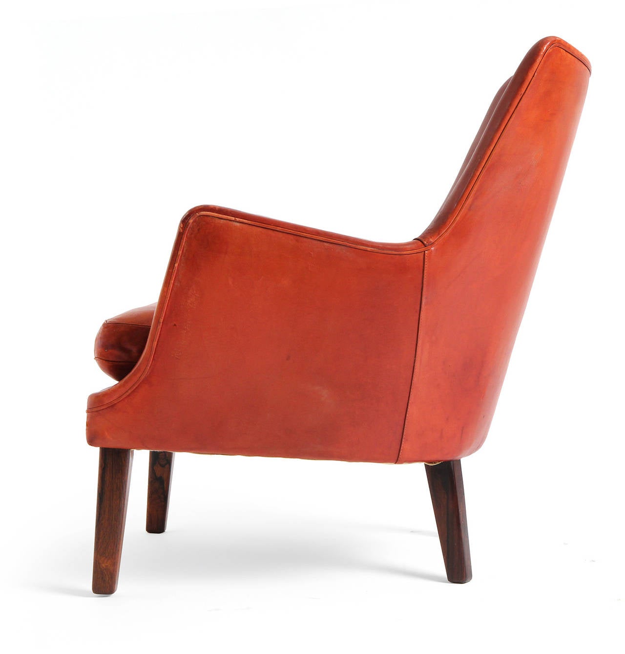 An uncommon, sculptural and wonderfully tactile lounge chair having a hand stitched natural leather body with inverted tufting and a generous down-filled cushion, floating on carved solid Brazilian rosewood legs.