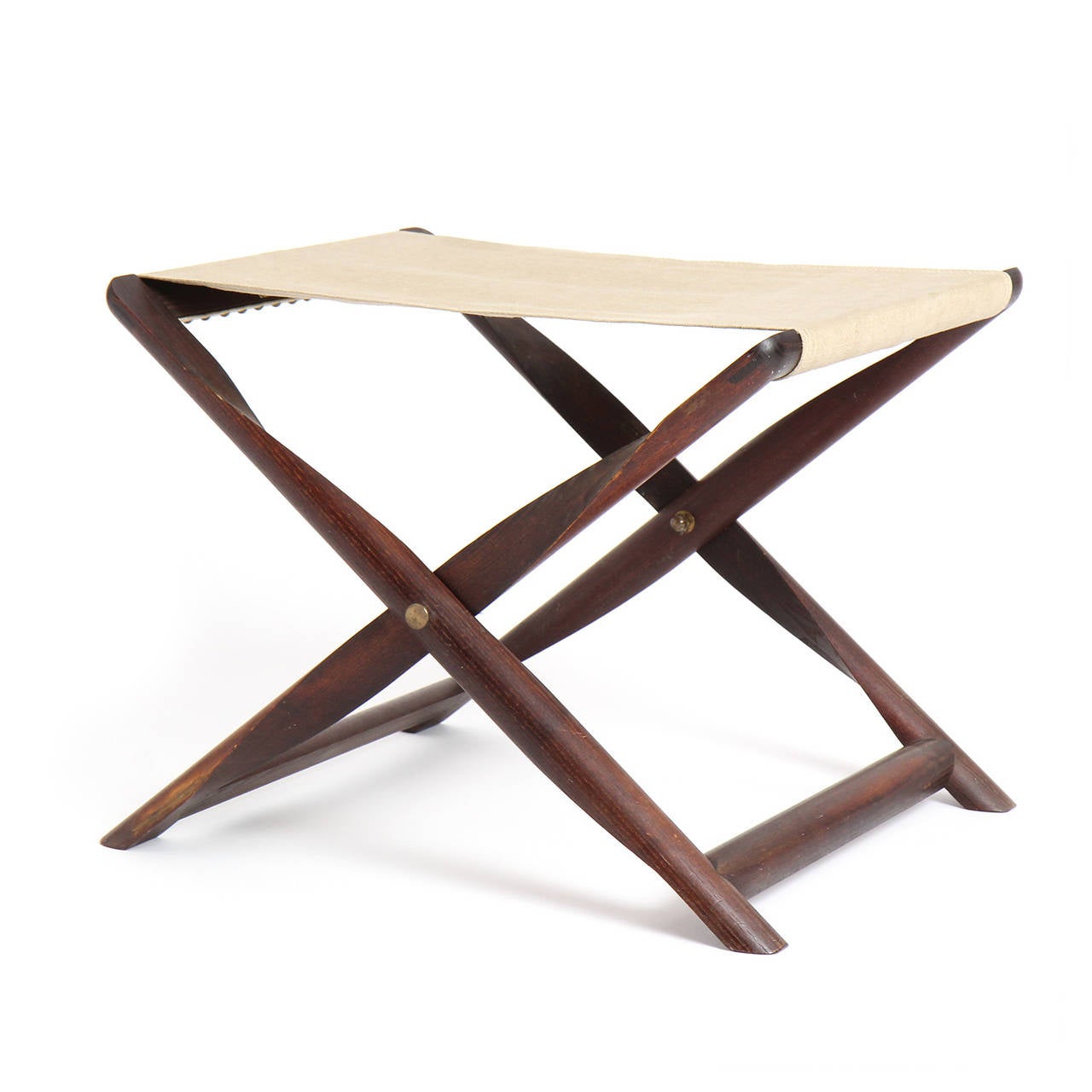 A beautiful hand crafted folding stool in rich mahogany having turned and sculpted propellor shaped intersecting legs with fine brass detailing and a hand stitched natural canvas sling seat attached with brass large head nails.
