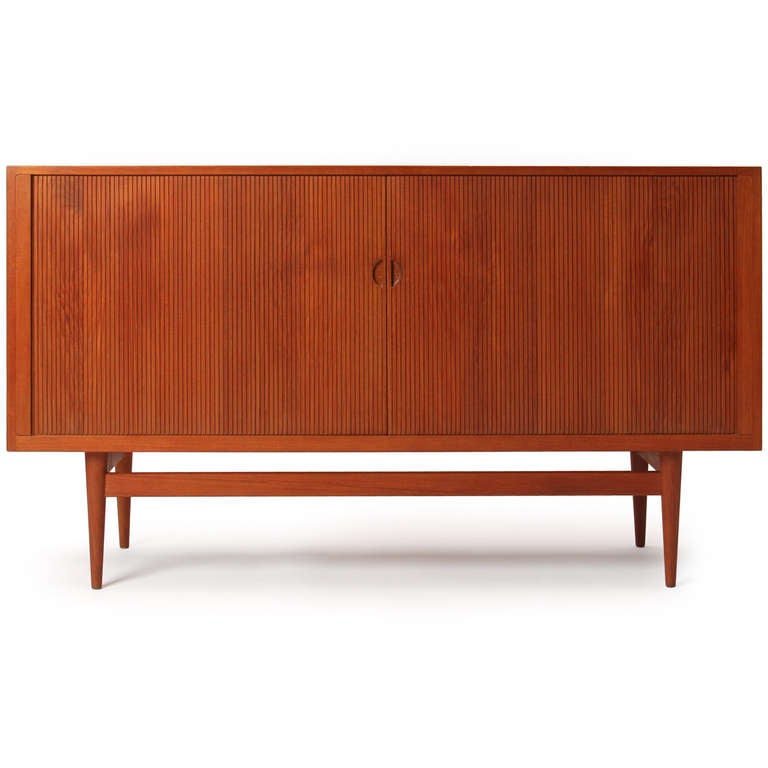 A tambour-doored credenza in teak (with fabulous storage), the case elevated on an architectural base with turned legs.