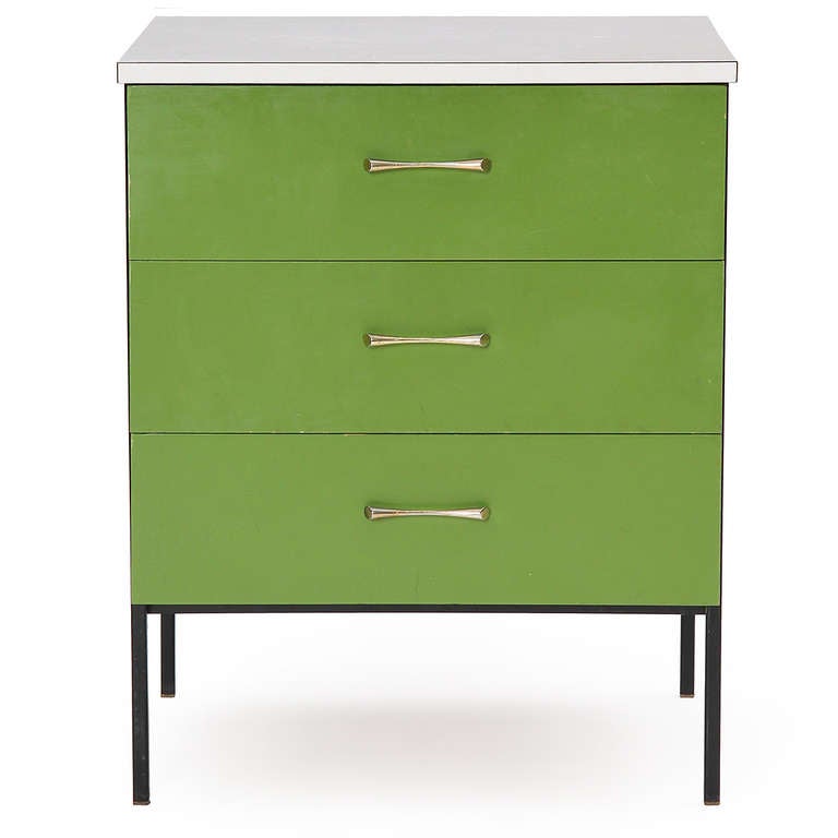A colorful nightstand with a black steel frame supporting three green lacquered drawers capped with a white laminate top.