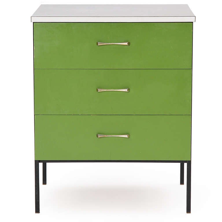 A colorful nightstand with a black steel frame supporting three green lacquered drawers capped with a white laminate top.