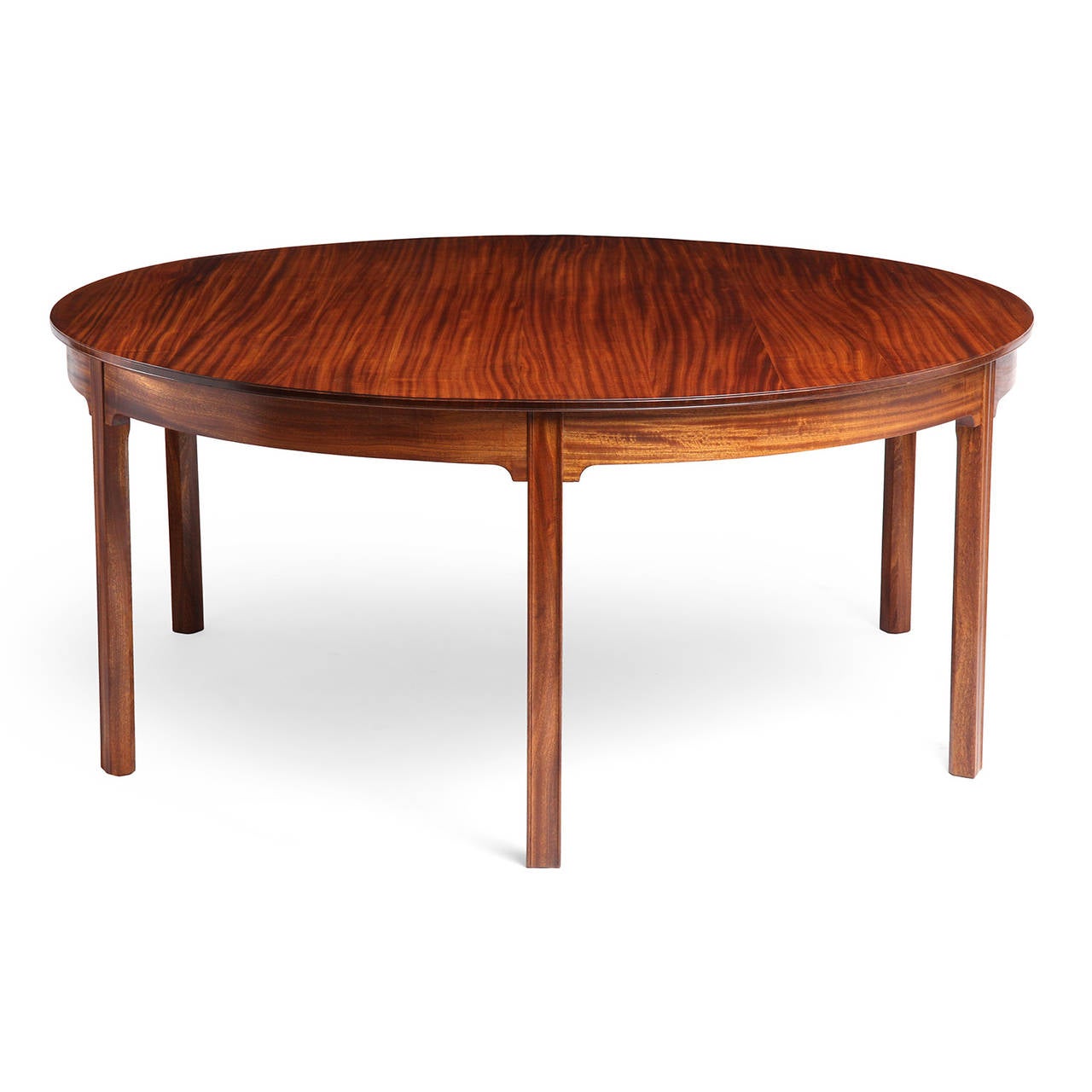 A rare, stately and superb dining table of fine proportion and refined and subtle neoclassical detailing. handcrafted of beautifully figured Honduran mahogany, the circular top has restrained arched aprons and floats upon six carved squared legs.