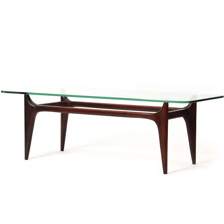 A rectangular low table on a tapered and sculpted base having a floating glass top.