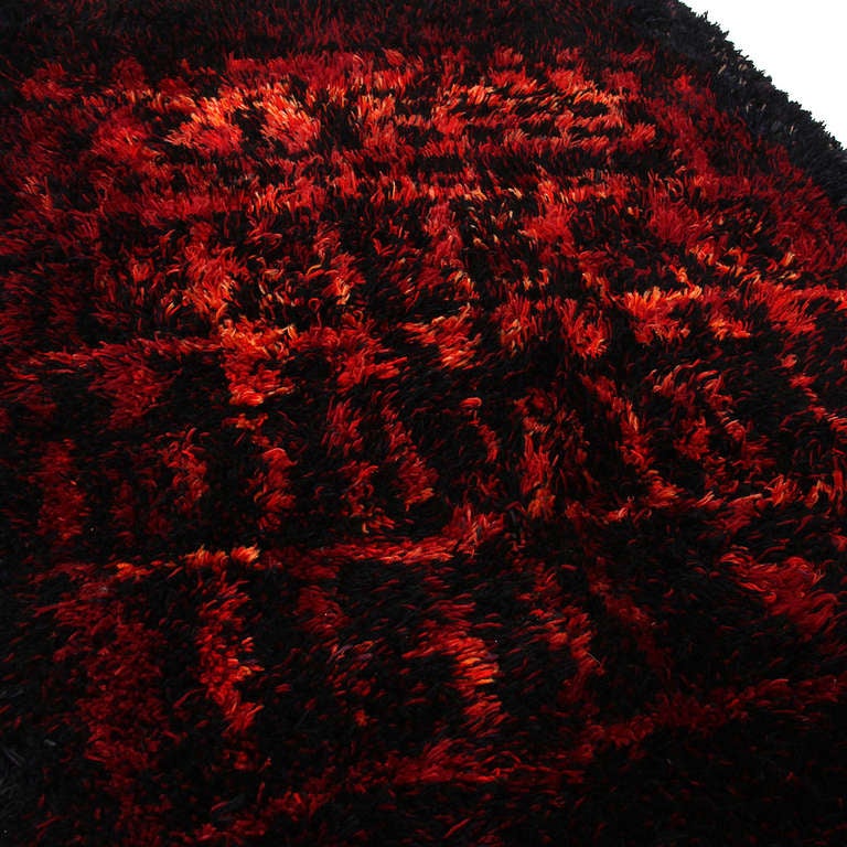 A wool rug woven and hand-knotted in shades of red, orange, blue and black.