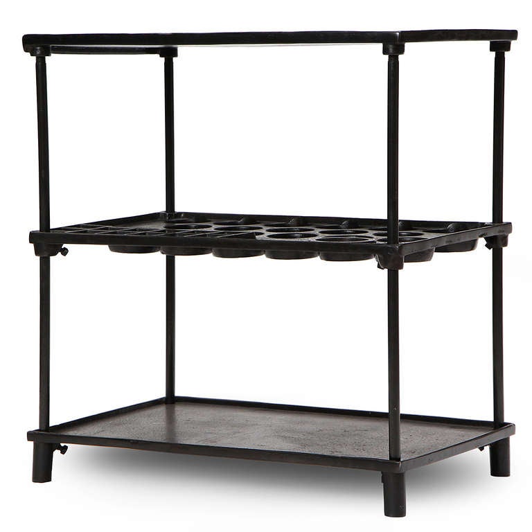 A three-tiered industrial table rendered in richly patinated steel and cast iron, having adjustable raised-edge shelves - the middle shelf inset with pockets and bolt trays.