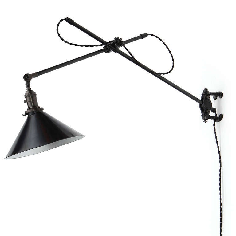 An early wall-mounted and fully articulated swing-arm lamp having a dark patinated finish, lacquered steel conical shade and an ornate cast iron wall plate.
