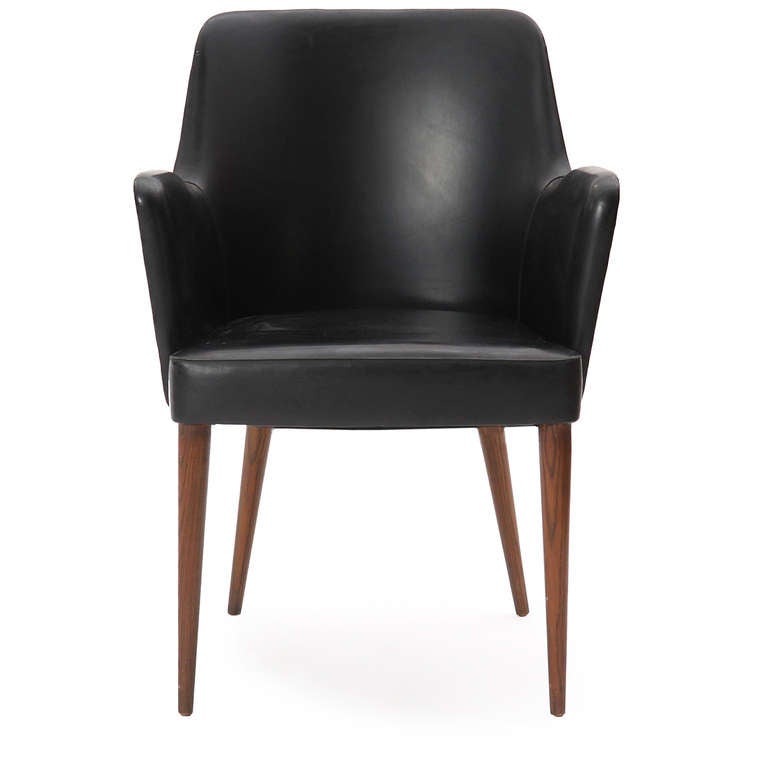 An elegant and uncommon arm or desk chair having a tailored and sculptural seat upholstered in black vinyl on flaring walnut turned-dowel legs.