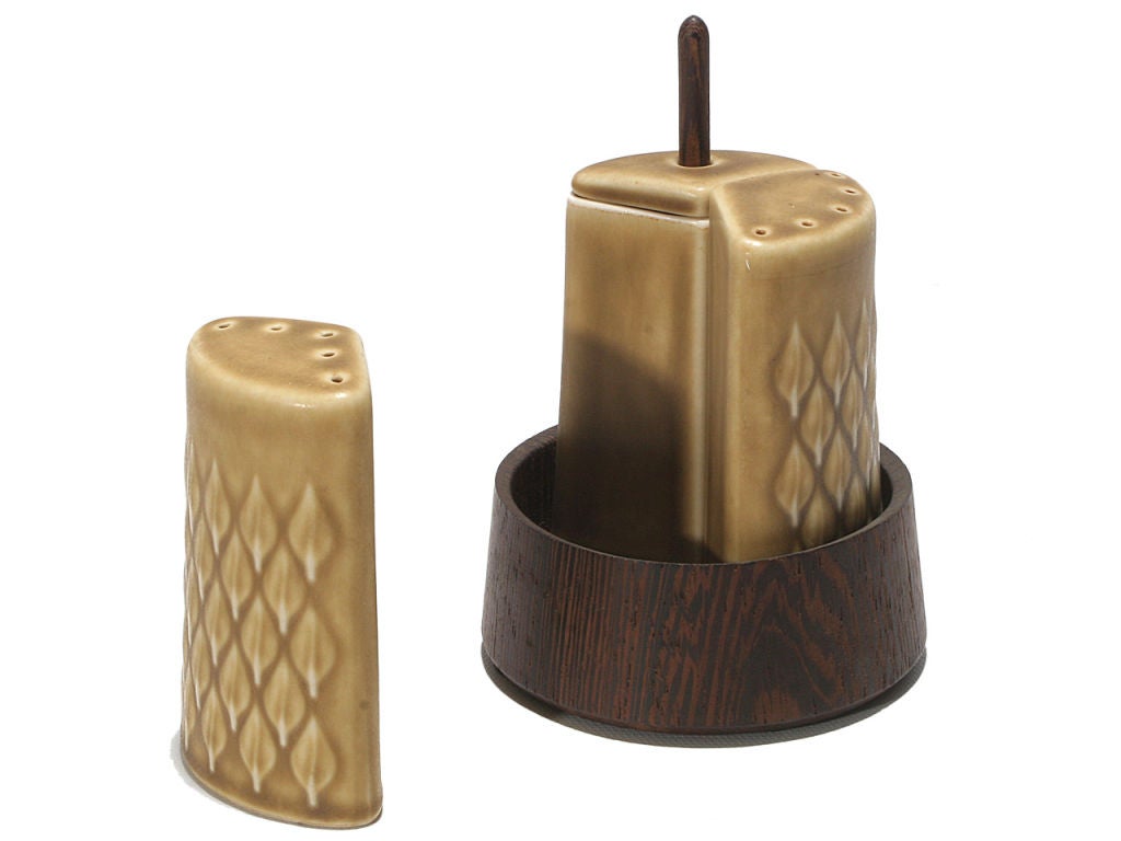 A textured ceramic set with a warm glaze consisting of salt and pepper shakers and a honey pot with dripper nestled in a wenge base.
  