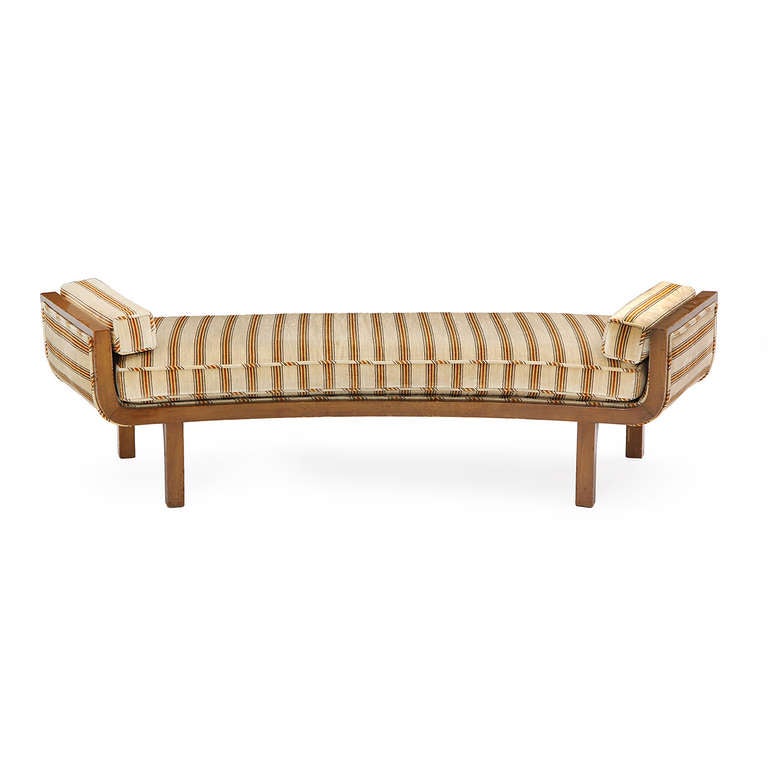 An elegant upholstered bench or small daybed having a distinctive curved upturned form in a banded walnut frame on squared legs.