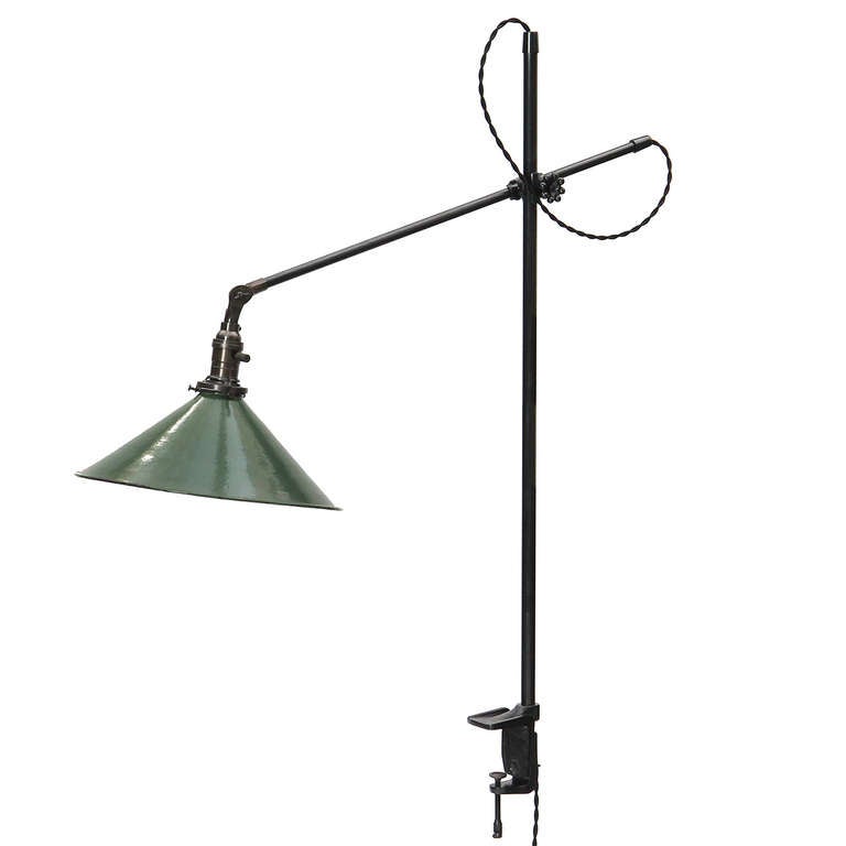 An articulated and adjustable desk lamp in cast iron and steel with a clamping foot for mounting to a desk or shelf and light reflecting from a green enameled cone shade.