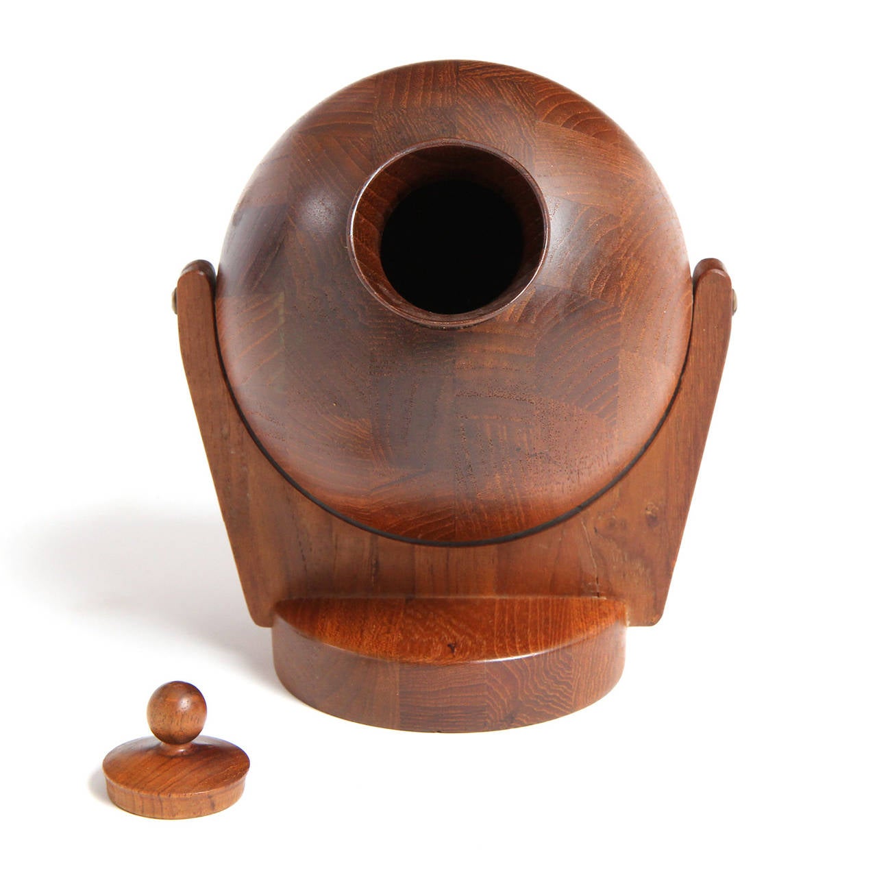 A wall-mounted lidded tobacco vessel having a rounded tilting form on mounted arms crafted of turned and carved richly figured teak.