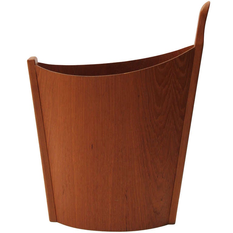 A Norwegian wastebasket having molded and shaped sides and a sculpted single handle in solid teak.