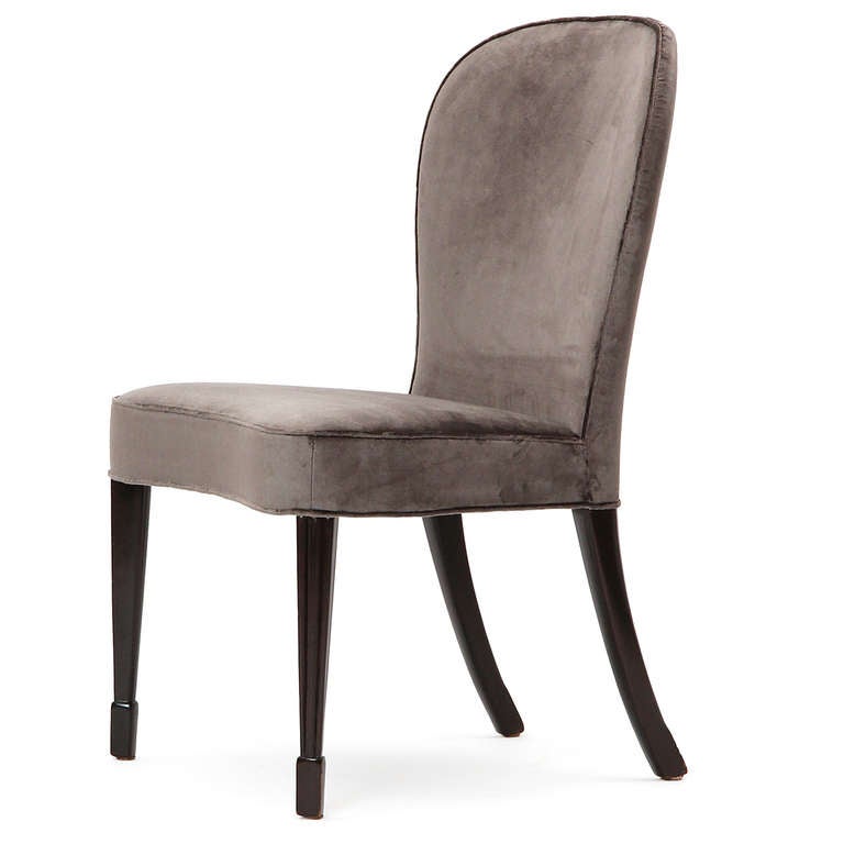 An elegant dining chair having sculpted tapering walnut legs and generous tailored seats upholstered in a light grey mohair.